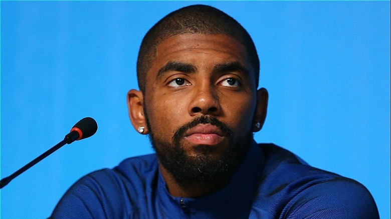 Kyrie Irving est assise devant un micro devant un fond bleu