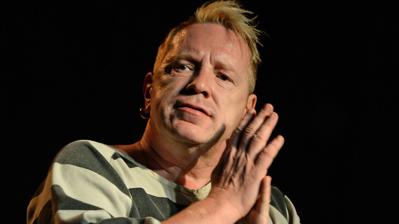 Johnny Rotten, dans une chemise de style prison, les mains jointes