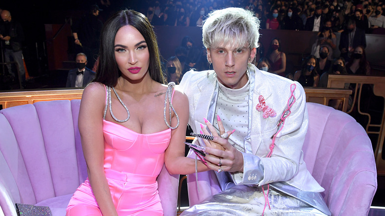 Megan Fox et Machine Gun Kelly assises sur un canapé rose.