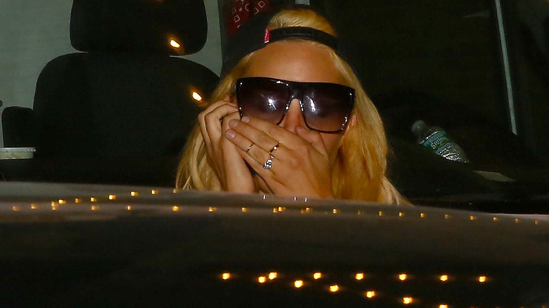 Amanda Bynes en casquette et lunettes de soleil, couvrant la bouche