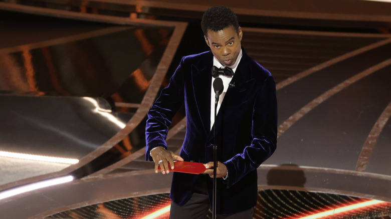 Chris Rock sur la scène des Oscars tenant une enveloppe