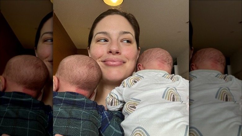 Ashley Graham souriant avec deux bébés sur ses épaules