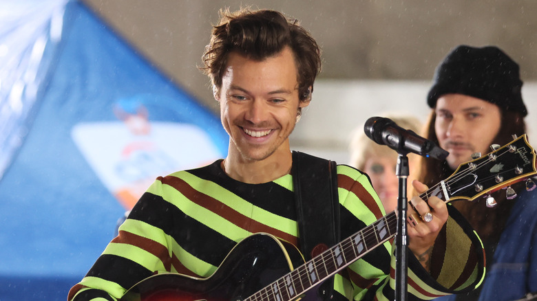 Harry Styles souriant en jouant de la guitare