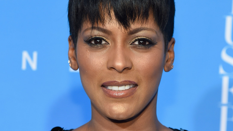 Tamron Hall devant un mur bleu, souriant