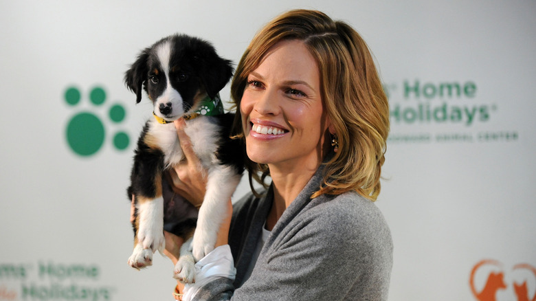 Hilary Swank sourit en tenant un chien