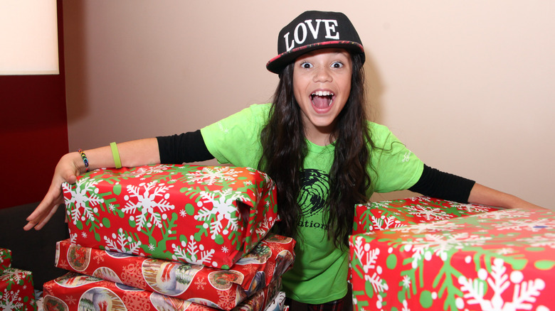 Une jeune Jenna Ortega tenant de gros cadeaux de Noël