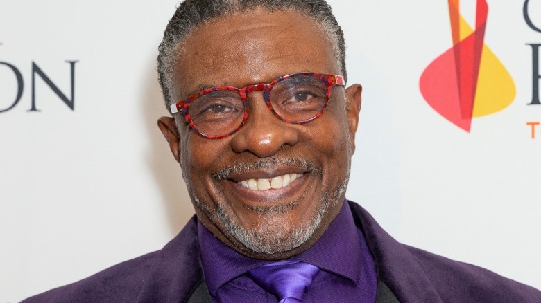 Keith David portant un costume et une cravate violets, souriant