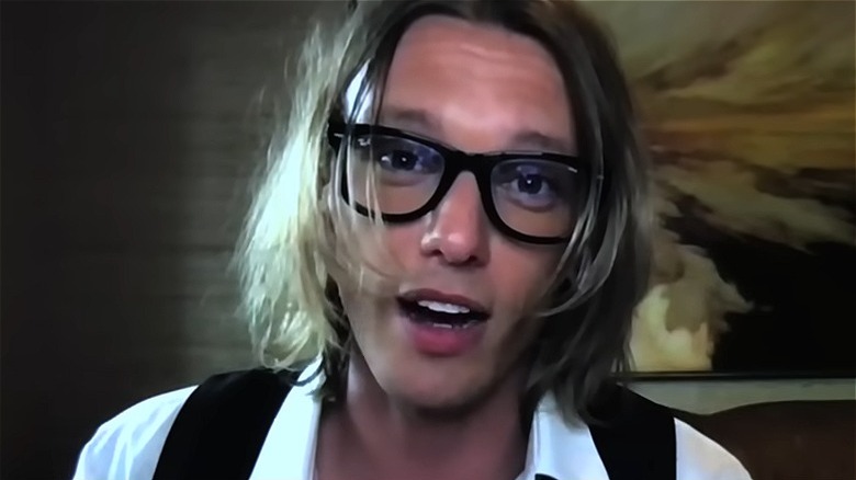 Jamie Campbell Bower portant des lunettes épaisses, parlant