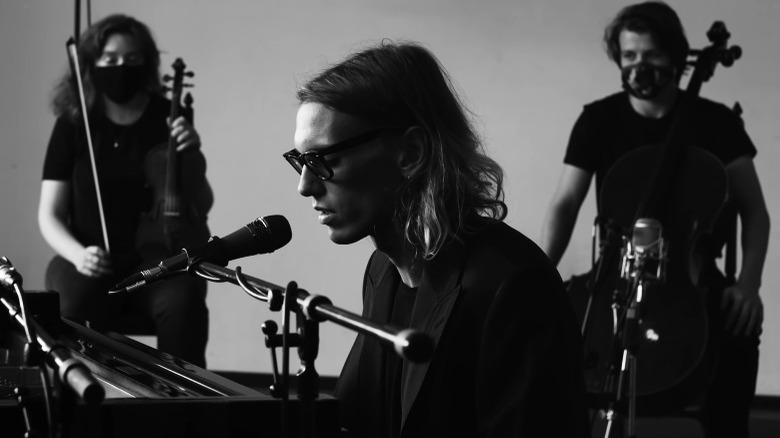 Jamie Campbell Bower au piano, deux musiciens derrière lui