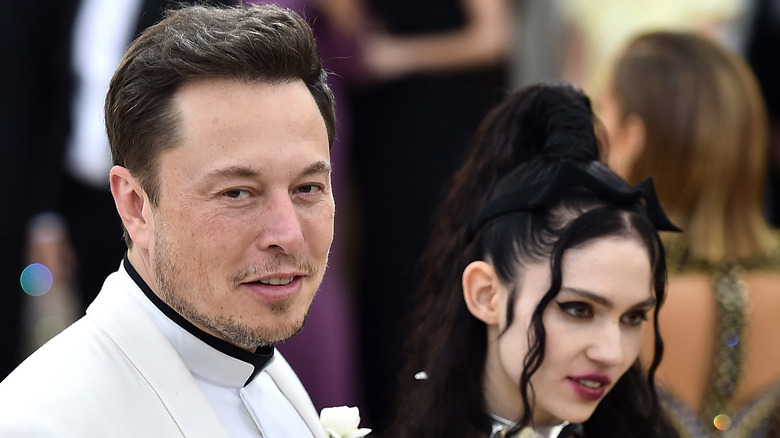 Elon Musk souriant barbe courte Grimes longs cheveux noirs