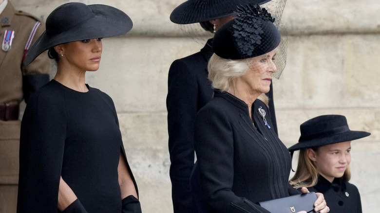 Camilla tenant un sac à main, avec Meghan Markle et la princesse Charlotte