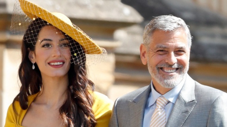 Amal Clooney en chapeau jaune et George Clooney souriant 