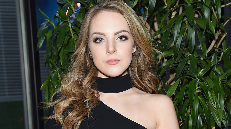 Liz Gillies avec de longs cheveux blonds sales ondulés et un haut noir avec tour de cou