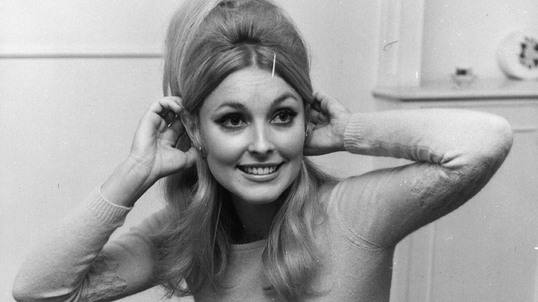 Sharon Tate souriante, ajustant ses cheveux