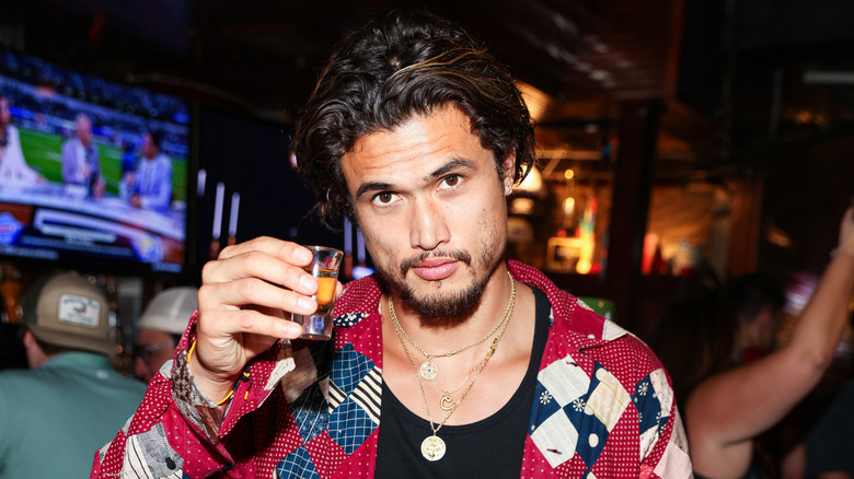 Charles Melton tenant un verre dans un bar