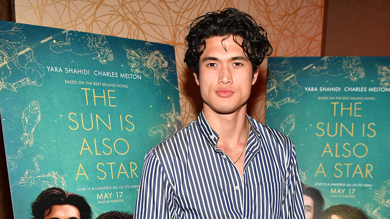 Charles Melton posant devant deux affiches de film pour Le Soleil est aussi une star