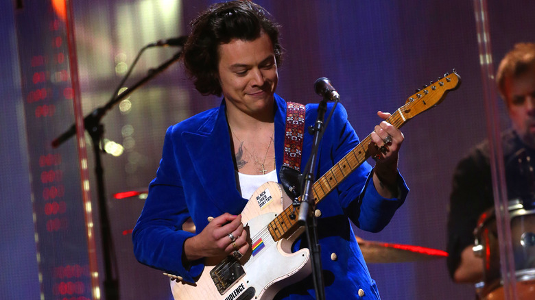 Harry Styles joue de la guitare dans un costume bleu Gucci