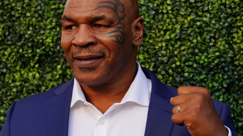 Mike Tyson lève le poing devant un mur de feuilles