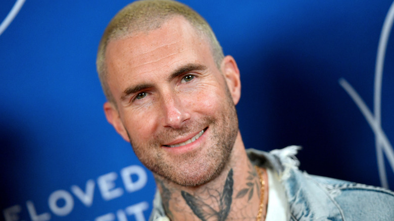 Adam Levine souriant avec le crâne rasé