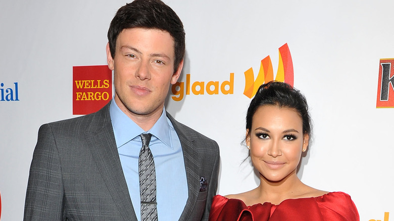 Cory Monteith tall costume gris cheveux noirs cravate Naya Rivera cheveux noirs robe rouge chignon bouche fermée sourit