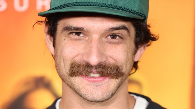 Tyler Posey souriant, moustache fond orange