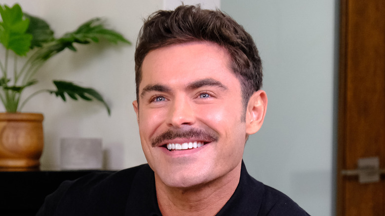 Zac Efron avec une moustache et souriant