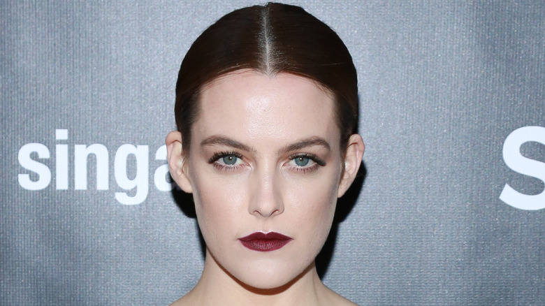 Riley Keough cheveux noirs lisses, rouge à lèvres foncé, l'air sérieux