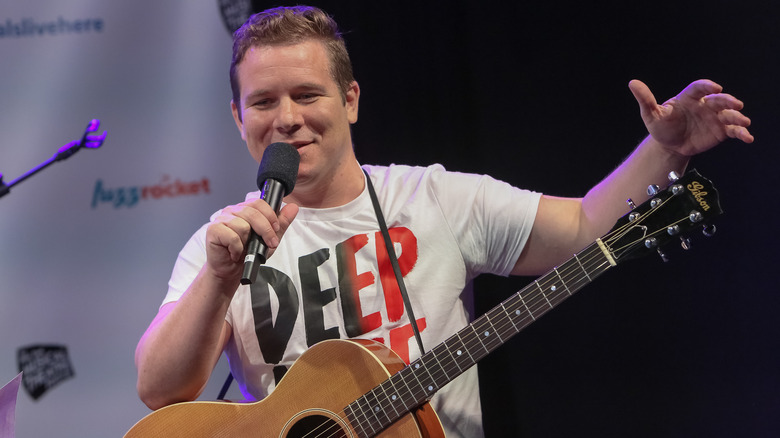 Jon Peter Lewis sur scène avec un microphone et une guitare