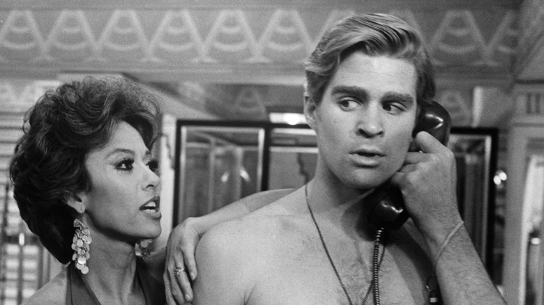 Un Treat Williams torse nu tenant un téléphone à côté de Rita Moreno