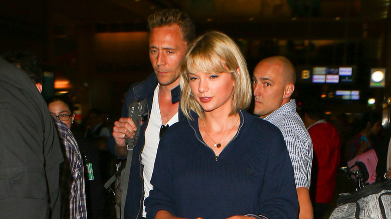 Tom Hiddleston fronçant les sourcils derrière Taylor Swift