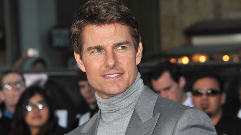 Tom Cruise souriant en costume gris et col roulé