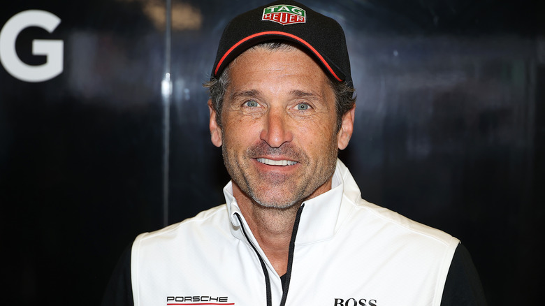 Patrick Dempsey posant avec un chapeau et un gilet Porsche