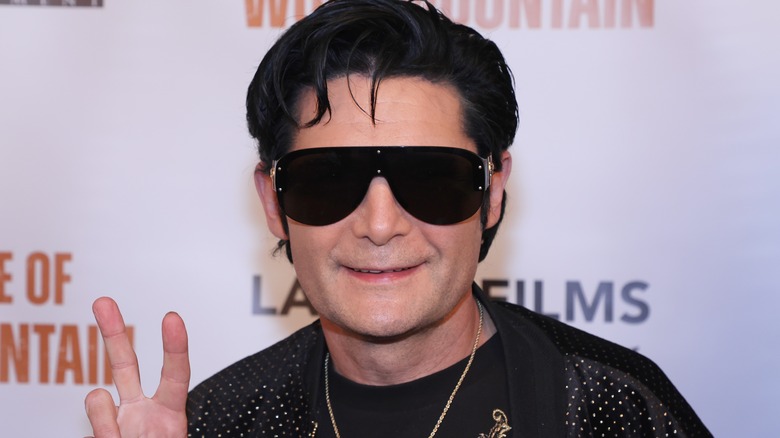 Corey Feldman sourit en signe de paix avec des lunettes de soleil