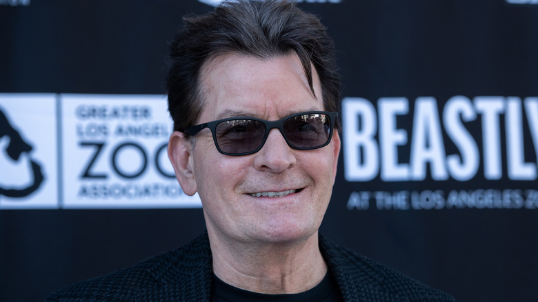 Charlie Sheen souriant avec des lunettes de soleil en 2023