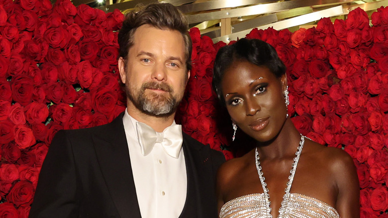 Joshua Jackson et Jodie Turner-Smith souriant ensemble devant un arrangement floral rouge