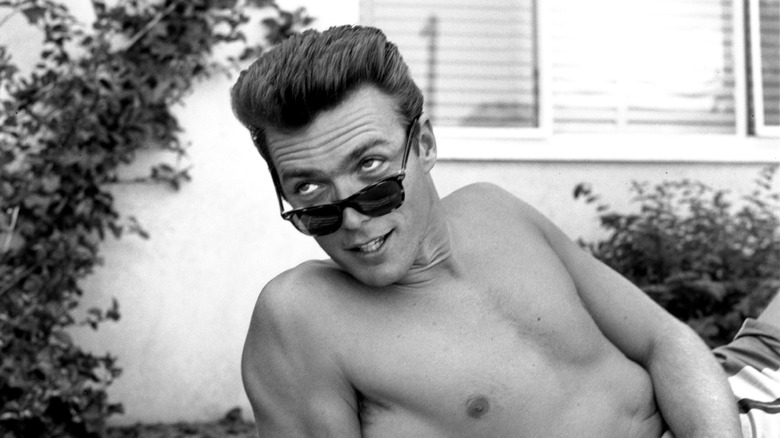 Clint Eastwood souriant à travers ses lunettes de soleil alors qu'il s'allonge, torse nu, dans les années 1950