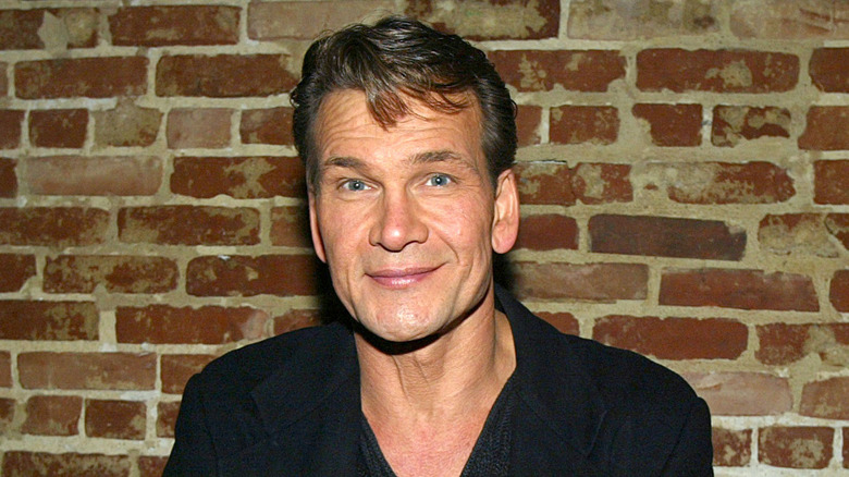 Patrick Swayze souriant mur de briques