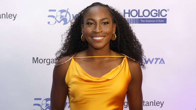 Coco Gauff souriante dans une robe moutarde