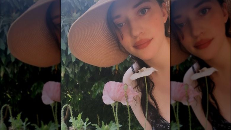 Kat Dennings posant avec un chapeau de soleil dans son jardin avec des fleurs de pavot