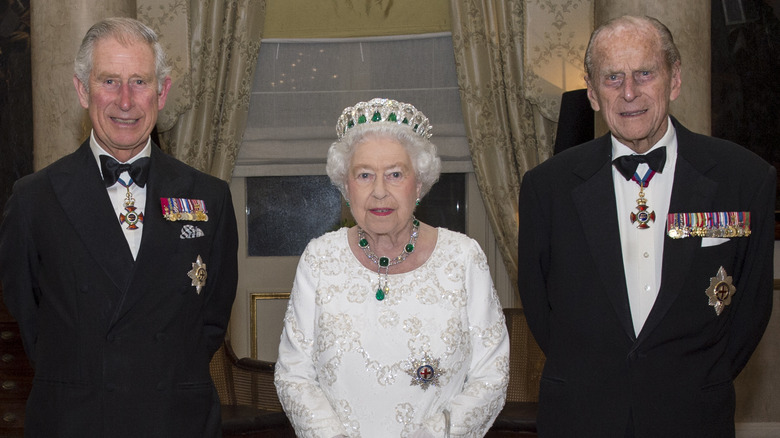 Le roi Charles souriant, la reine portant une couronne, le prince Philip grimaçant