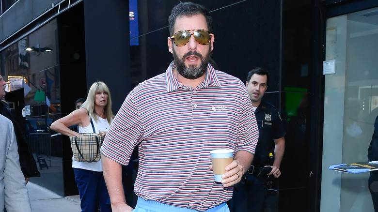 Adam Sandler tenant un café sur un trottoir