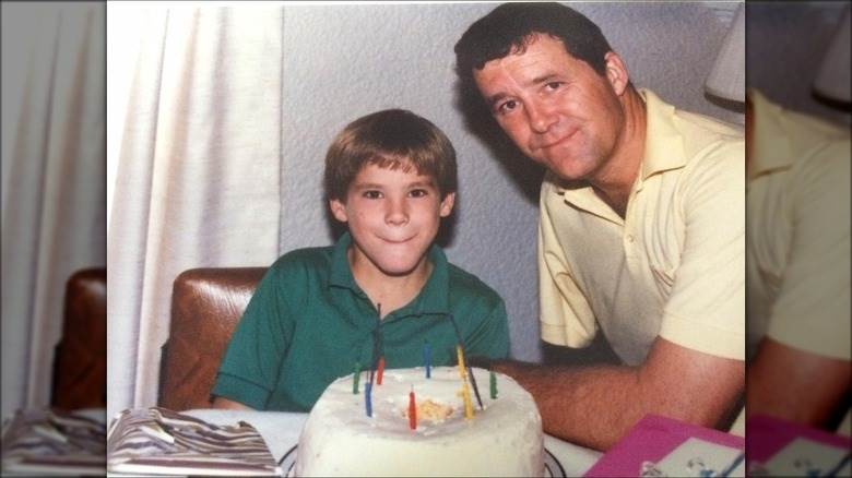 Un jeune Ryan Reynolds souriant avec son père devant un gâteau d'anniversaire