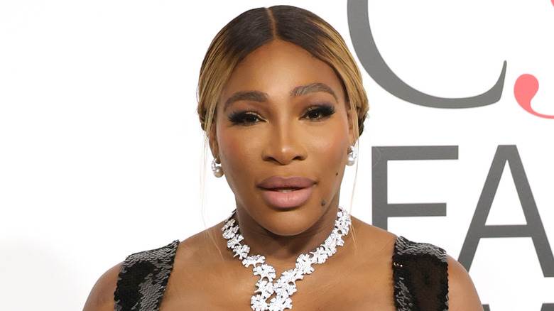 Serena Williams posant sur le tapis rouge avec un collier argenté et une robe noire