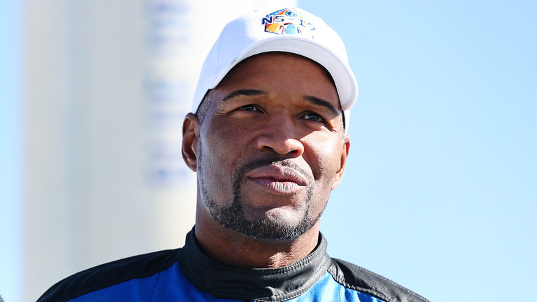 Michael Strahan posant avec une casquette blanche et une veste bleue