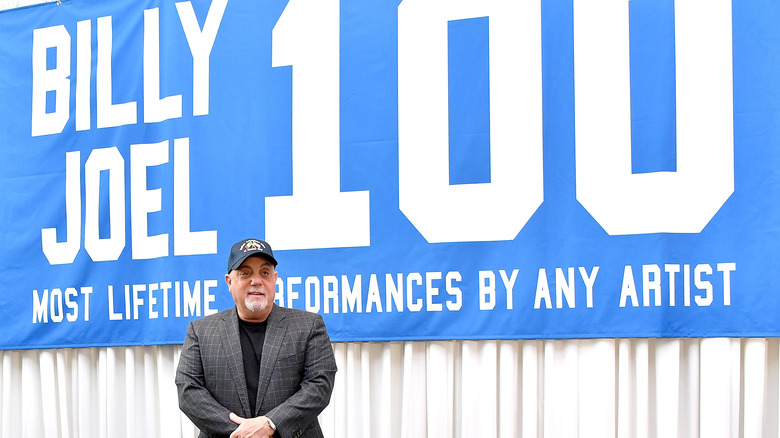 Billy Joel se tient devant la bannière « Billy Joel 100 »