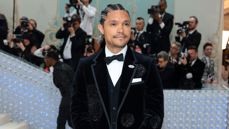 Trevor Noah souriant lors d'un événement sur le tapis rouge avec des cornrows