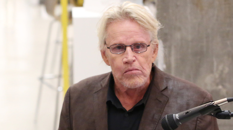 Gary Busey parlant dans un microphone avec des lunettes