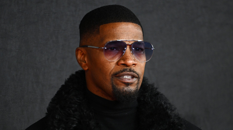 Jamie Foxx posant en lunettes de soleil et manteau noir