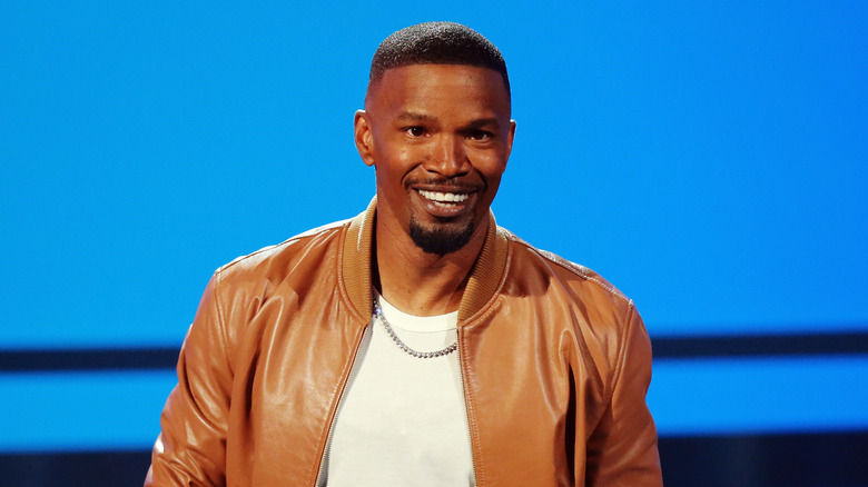 Jamie Foxx souriant posant dans une chemise blanche et une veste marron clair