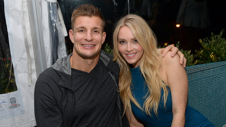 Rob Gronkowski portant une veste grise et un t-shirt gris avec Camille Kostek portant une robe sans manches à col montant bleu sarcelle